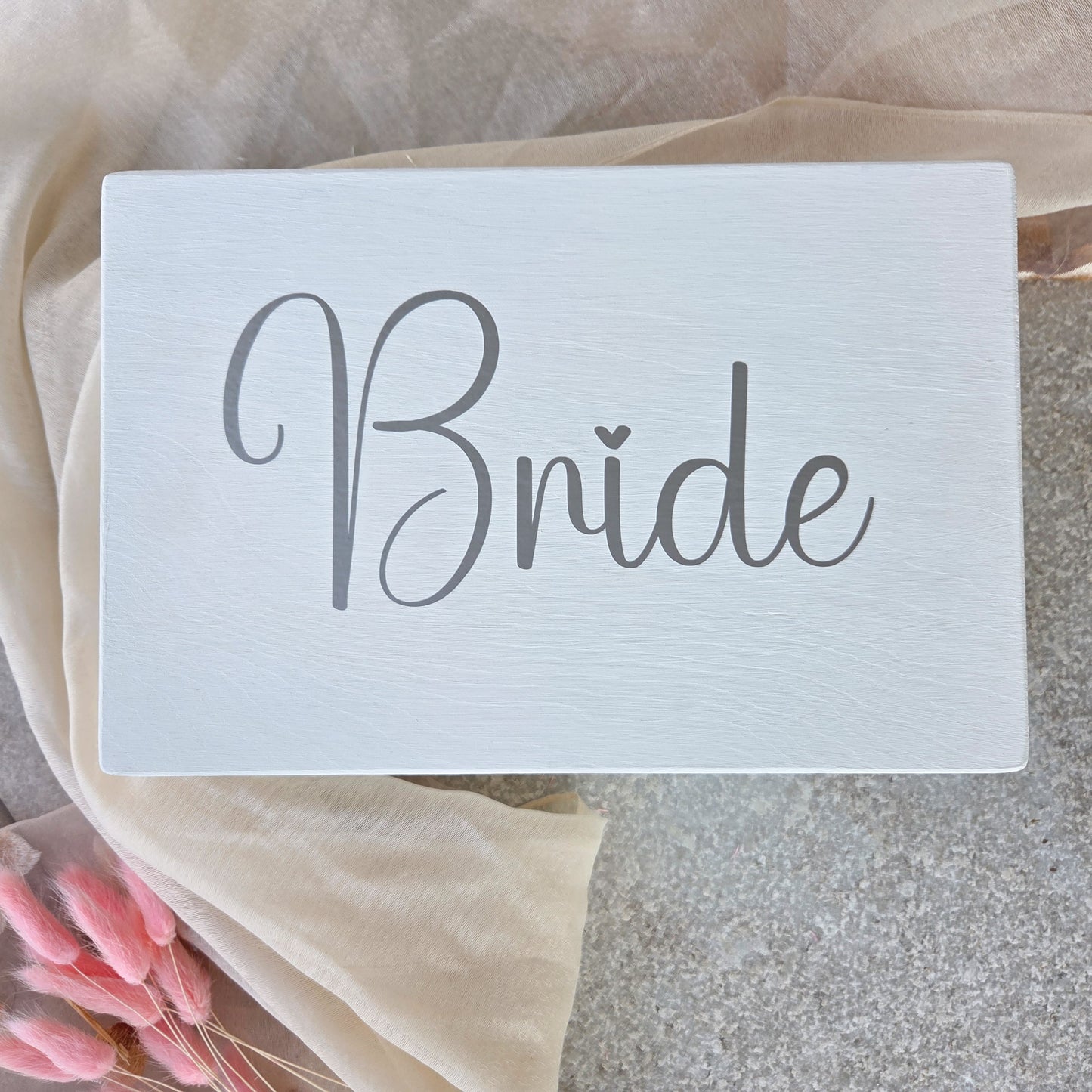 Weisse Braut-Erinnerungsbox mit grossem Schriftzug „Bride“ auf dem Deckel, dekorativ auf hellem Tuch arrangiert als stilvolles Hochzeits-Andenken.