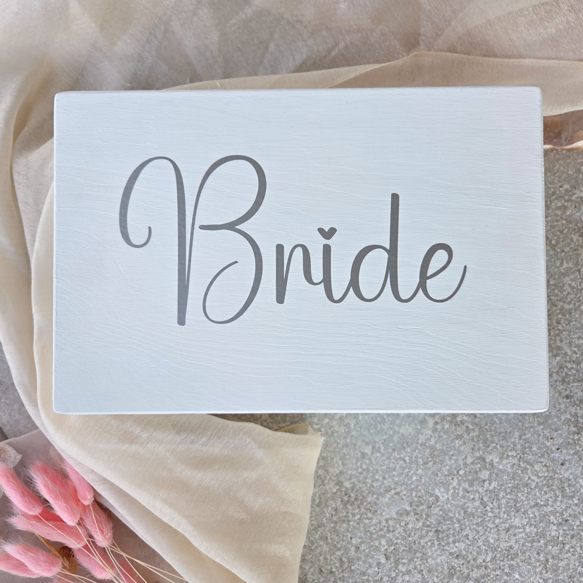Weisse Braut-Erinnerungsbox mit grossem Schriftzug „Bride“ auf dem Deckel, dekorativ auf hellem Tuch arrangiert als stilvolles Hochzeits-Andenken.