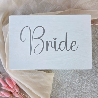Weisse Braut-Erinnerungsbox mit grossem Schriftzug „Bride“ auf dem Deckel, dekorativ auf hellem Tuch arrangiert als stilvolles Hochzeits-Andenken.