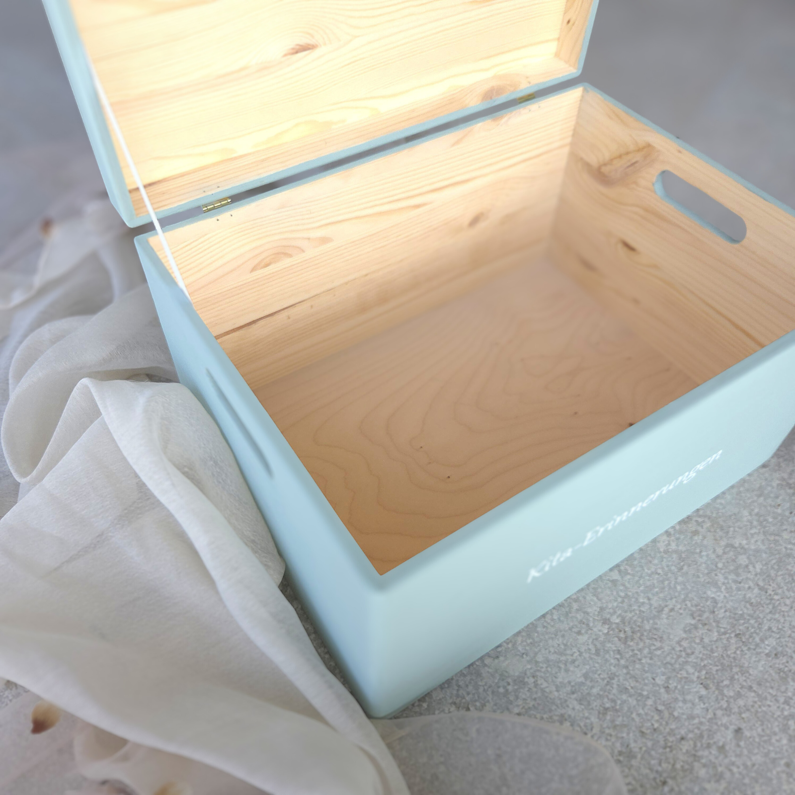 Geöffnete hellblaue Kita-Erinnerungsbox aus Holz mit grossem Innenraum, sichtbarer Holzmaserung und seitlichen Tragegriffen, ideal zur Aufbewahrung von Kita-Erinnerungen und Portfolio.