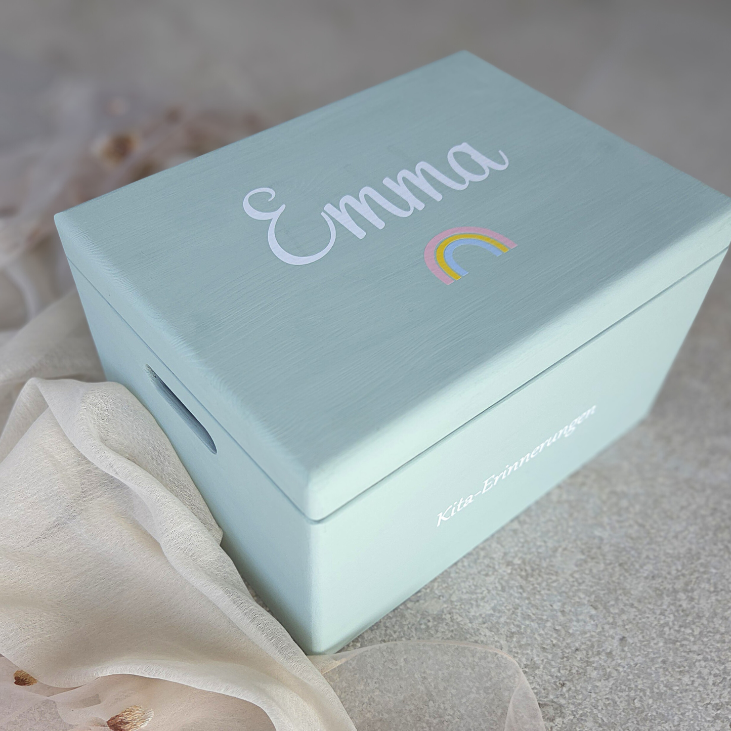 Hellblaue Kita-Erinnerungsbox aus Holz mit dem Namen „Emma“ und buntem Regenbogenmotiv auf dem Deckel sowie der Aufschrift „Kita-Erinnerungen“ an der Seite.