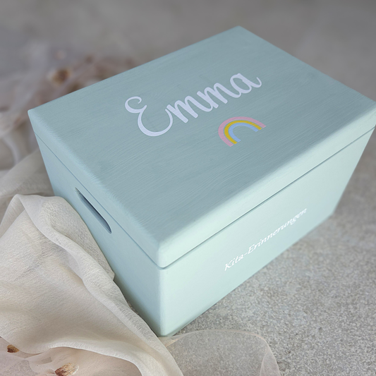 Hellblaue Kita-Erinnerungsbox aus Holz mit dem Namen „Emma“ und buntem Regenbogenmotiv auf dem Deckel sowie der Aufschrift „Kita-Erinnerungen“ an der Seite.