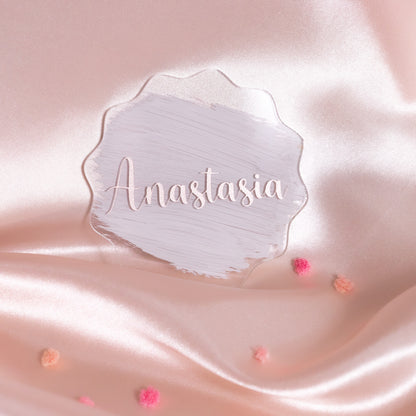 Rundes Acryl-Namensschild mit altrosa Brush-Hintergrund und dem Namen „Anastasia“ in eleganter Schrift, dekorativ auf roséfarbenem Satin mit kleinen Blüten.