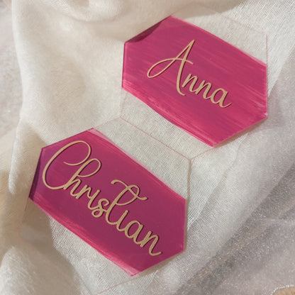 Personalisierte pinke Acryl-Namensschilder mit goldener Schrift für Anna und Christian auf hellem Stoffhintergrund als stilvolle Tischkarten.